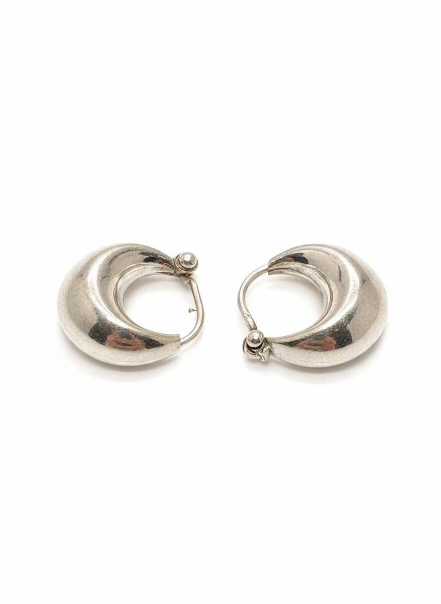 A close-up shot of a pair of sterling silver earrings hanging from a display, showing the sleek, reflective surface and the delicate ear wire.